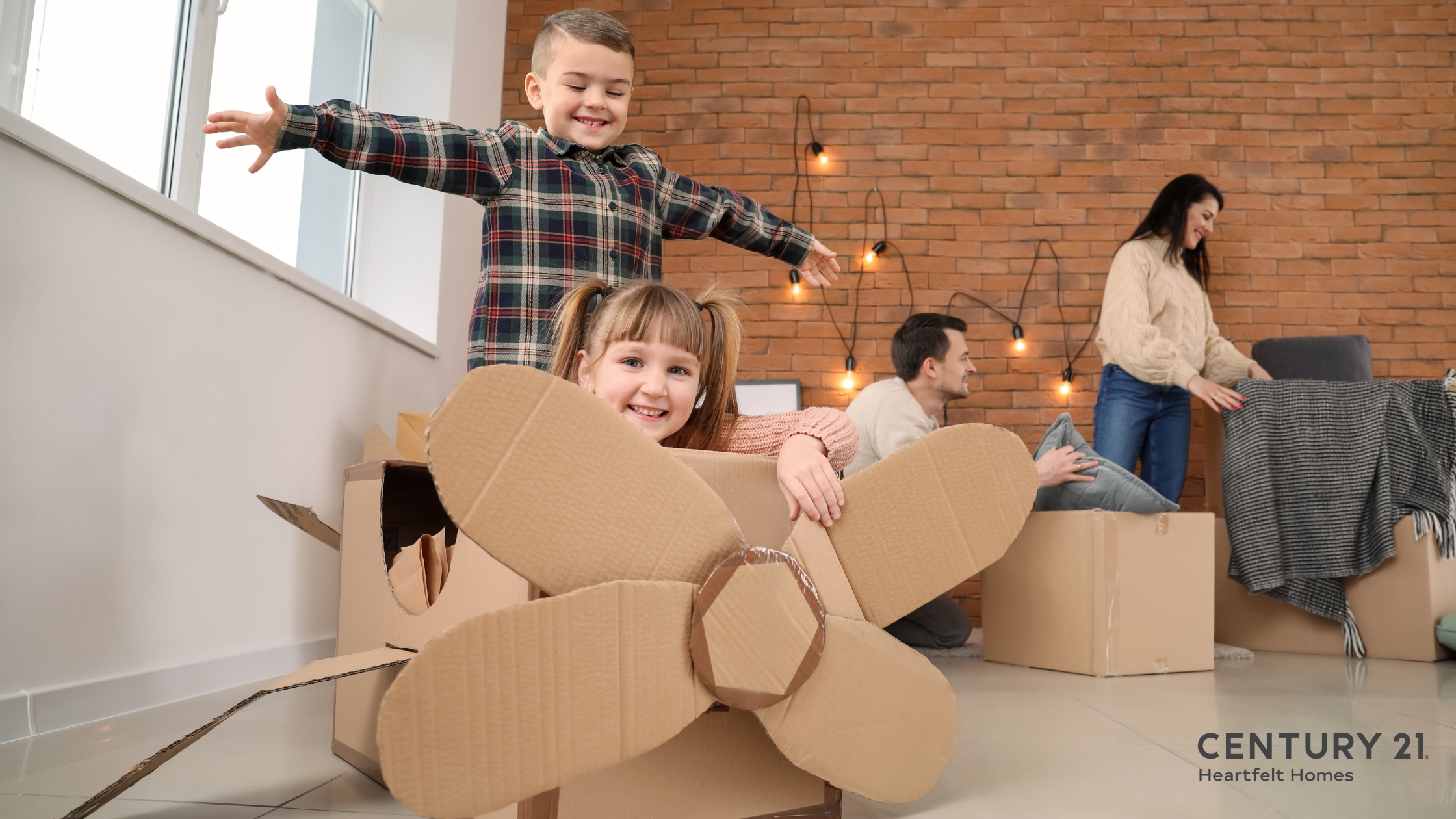 Young children playing in a cardboard box airplane while their parents unpack moving boxes