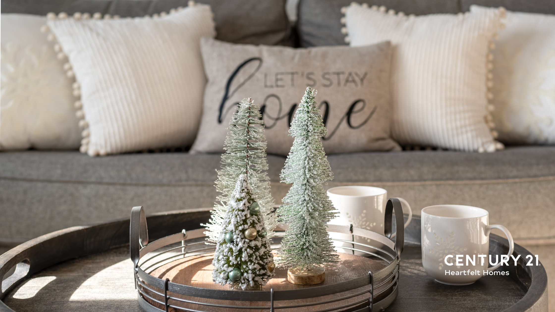 Gray couch with a "lets stay home pillow" behind a table with neutral winter decor.